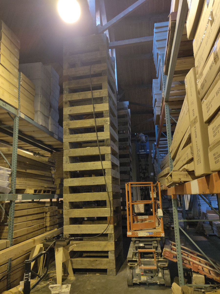 Timber cribbing tower shoring a warehouse interior between pallet racking